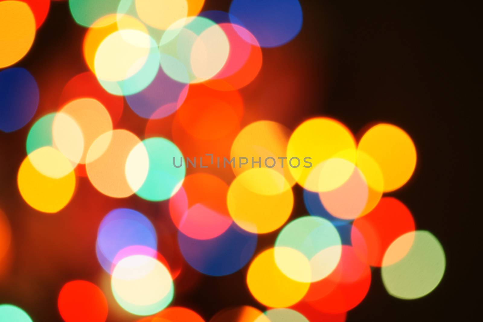 Multi-color holiday garland. Garland is blurred. Many colorful round lights. Fully defocused photo. Blurred background and foreground. Holiday mood. New Year and Christmas is coming.