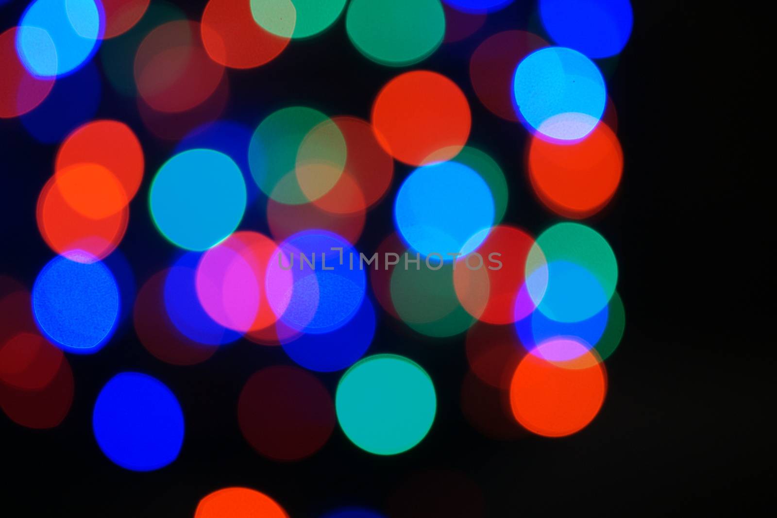 Multi-color blue holiday garland. Garland is blurred. Many big colorful round lights. Fully defocused photo. Blurred background and foreground. Holiday mood. New Year and Christmas is coming.