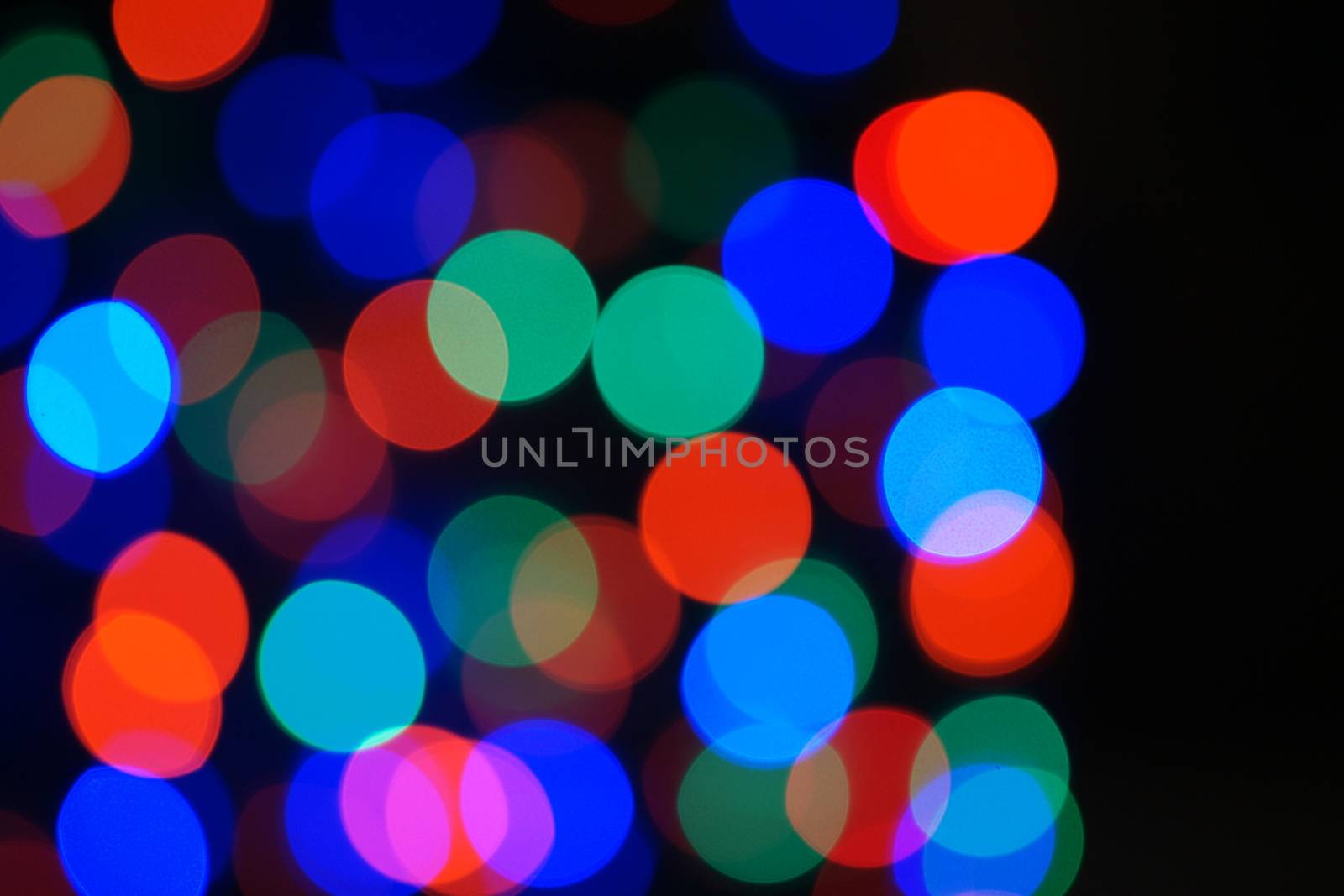 Multi-color blue holiday garland. Garland is blurred. Many big colorful round lights. Fully defocused photo. Blurred background and foreground. Holiday mood. New Year and Christmas is coming.