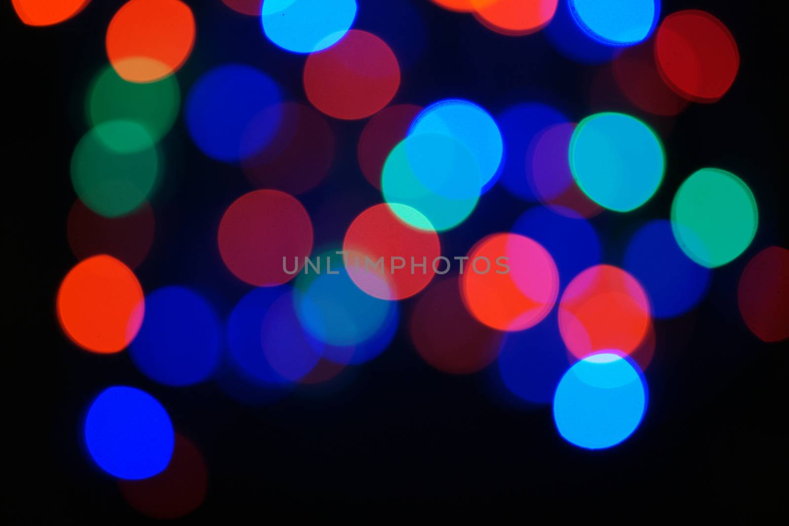 Multi-color blue holiday garland. Garland is blurred. Many big colorful round lights. Fully defocused photo. Blurred background and foreground. Holiday mood. New Year and Christmas is coming.