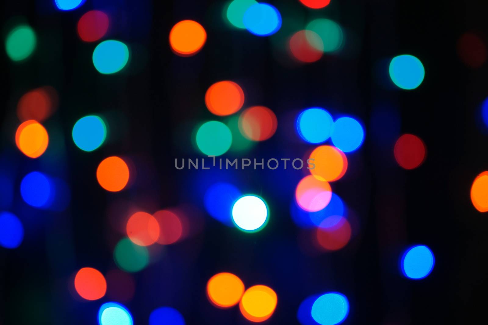 Multi-color blue holiday garland. Garland is blurred. Many big colorful round lights. Fully defocused photo. Blurred background and foreground. Holiday mood. New Year and Christmas is coming.