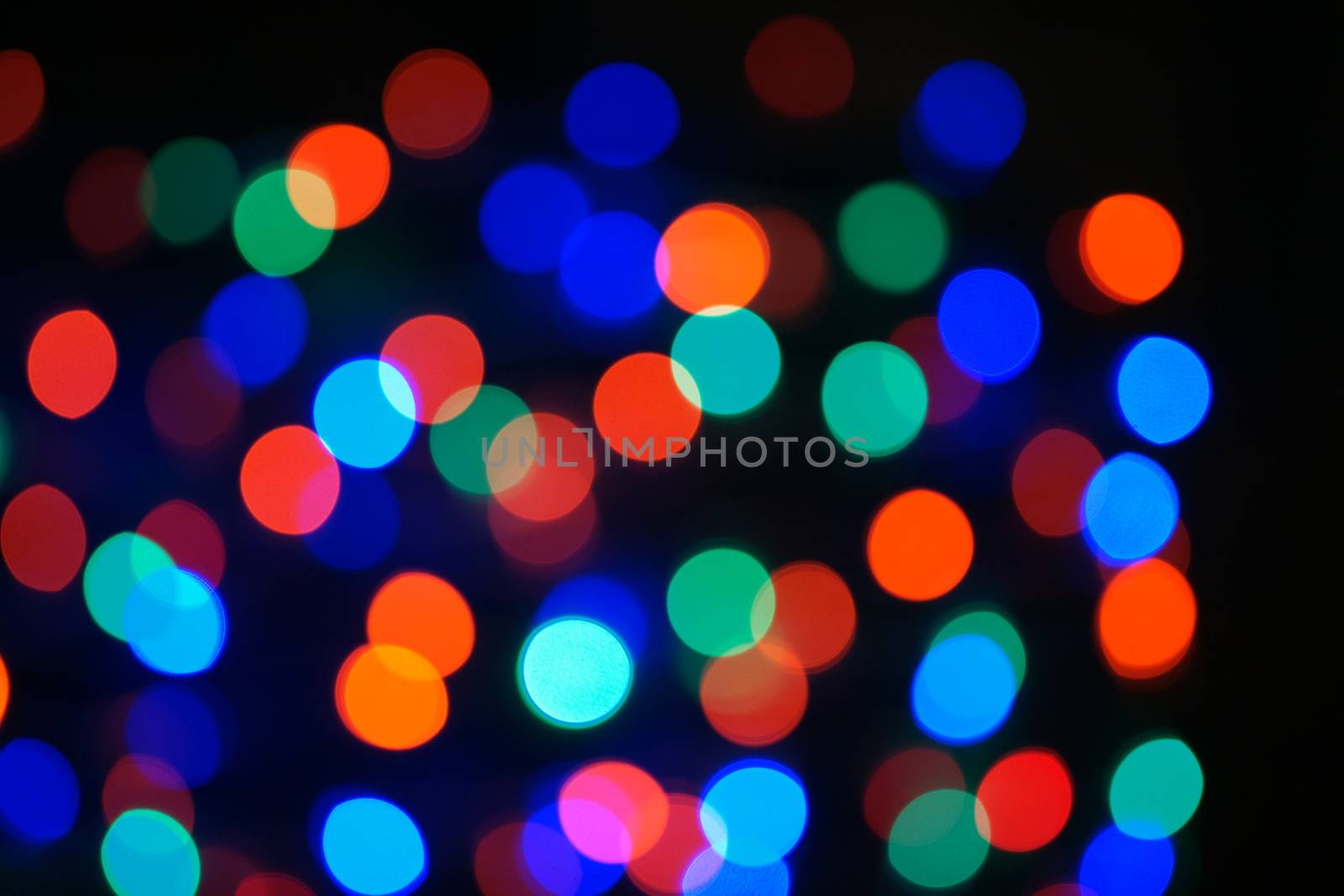 Multi-color blue holiday garland. Garland is blurred. Many big colorful round lights. Fully defocused photo. Blurred background and foreground. Holiday mood. New Year and Christmas is coming.