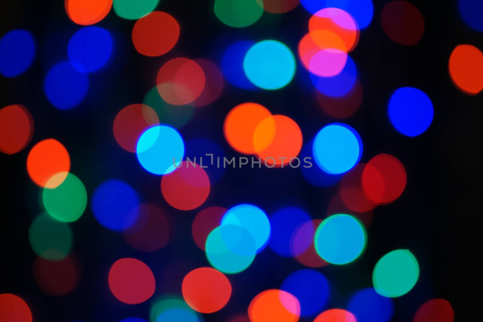 Multi-color blue holiday garland. Garland is blurred. Many big colorful round lights. Fully defocused photo. Blurred background and foreground. Holiday mood. New Year and Christmas is coming.