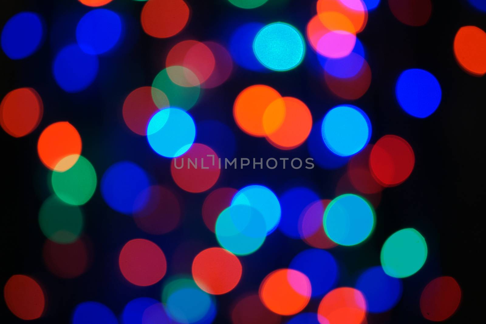 Multi-color blue holiday garland. Garland is blurred. Many big colorful round lights. Fully defocused photo. Blurred background and foreground. Holiday mood. New Year and Christmas is coming.