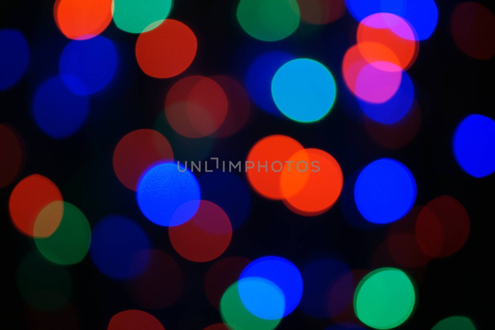 Multi-color blue holiday garland. Garland is blurred. Many big colorful round lights. Fully defocused photo. Blurred background and foreground. Holiday mood. New Year and Christmas is coming.