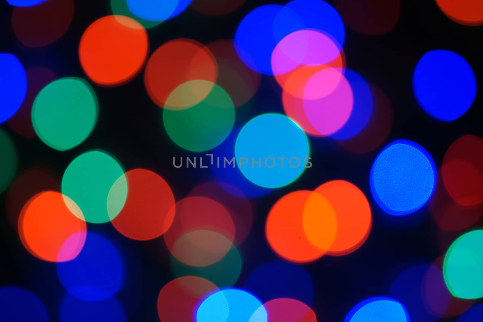Multi-color blue holiday garland. Garland is blurred. Many big colorful round lights. Fully defocused photo. Blurred background and foreground. Holiday mood. New Year and Christmas is coming.