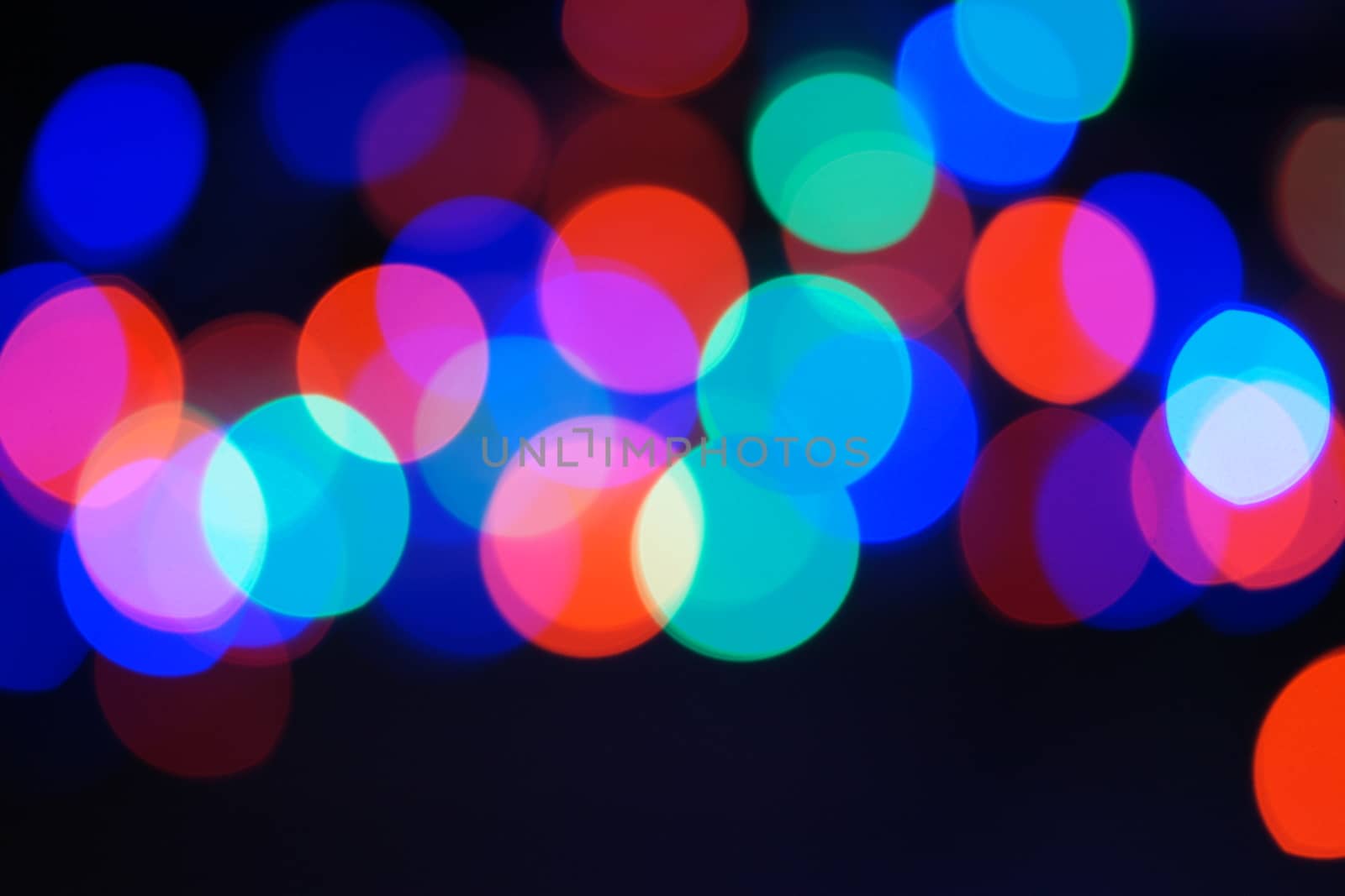 Multi-color blue holiday garland. Garland is blurred. Many big colorful round lights. Fully defocused photo. Blurred background and foreground. Holiday mood. New Year and Christmas is coming.