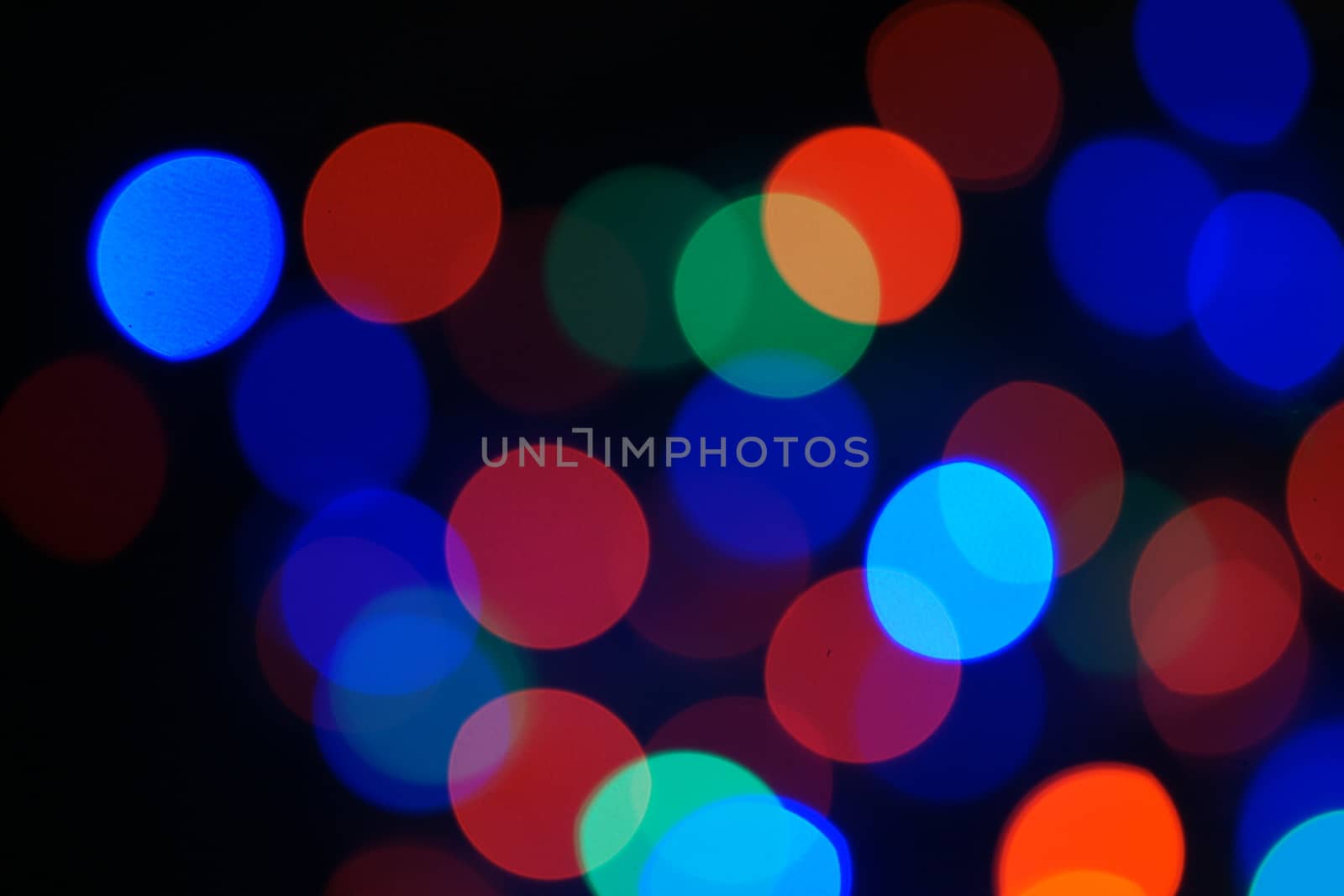 Multi-color blue holiday garland. Garland is blurred. Many big colorful round lights. Fully defocused photo. Blurred background and foreground. Holiday mood. New Year and Christmas is coming.