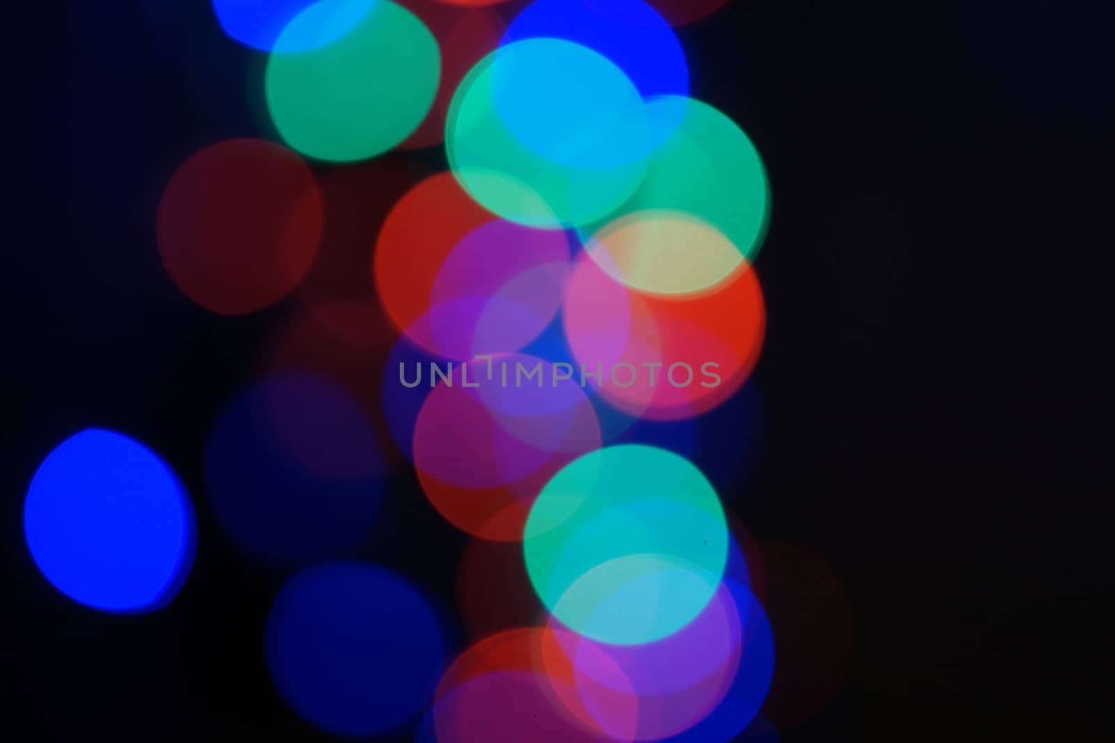 Multi-color blue holiday garland. Garland is blurred. Many big colorful round lights. Fully defocused photo. Blurred background and foreground. Holiday mood. New Year and Christmas is coming.