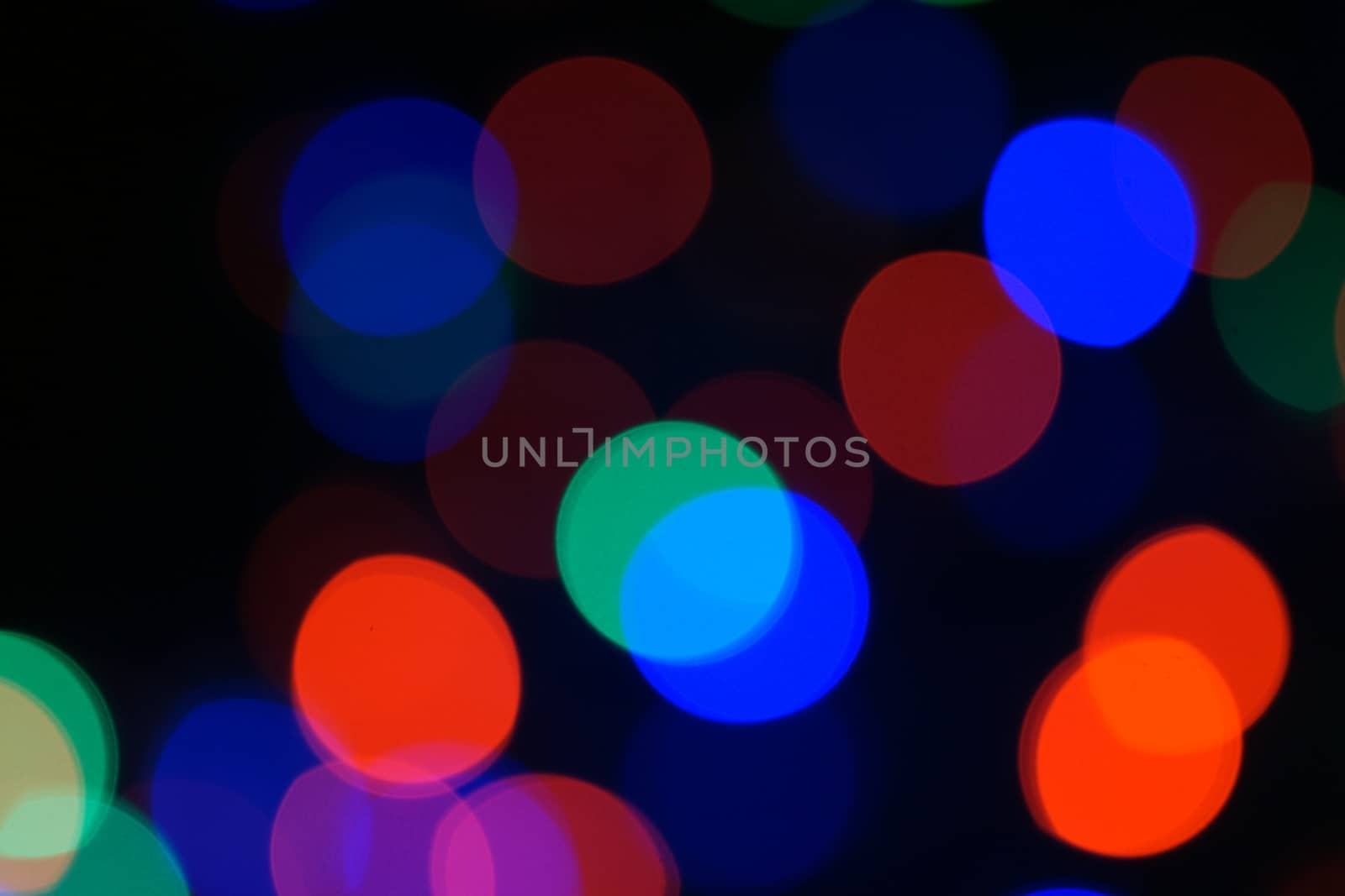 Multi-color blue holiday garland. Garland is blurred. Many big colorful round lights. Fully defocused photo. Blurred background and foreground. Holiday mood. New Year and Christmas is coming.