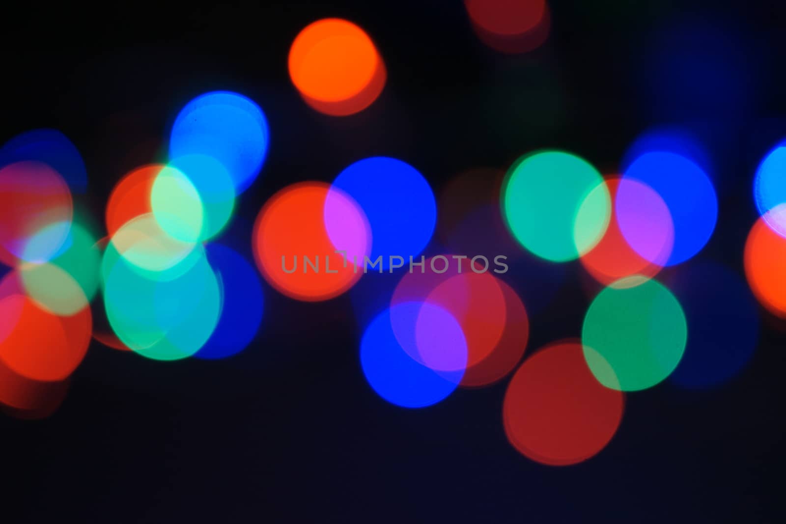 Multi-color blue holiday garland. Garland is blurred. Many big colorful round lights. Fully defocused photo. Blurred background and foreground. Holiday mood. New Year and Christmas is coming.