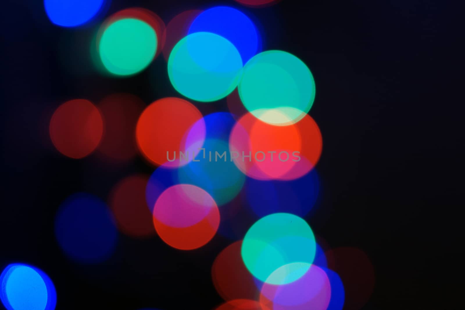 Multi-color blue holiday garland. Garland is blurred. Many big colorful round lights. Fully defocused photo. Blurred background and foreground. Holiday mood. New Year and Christmas is coming.