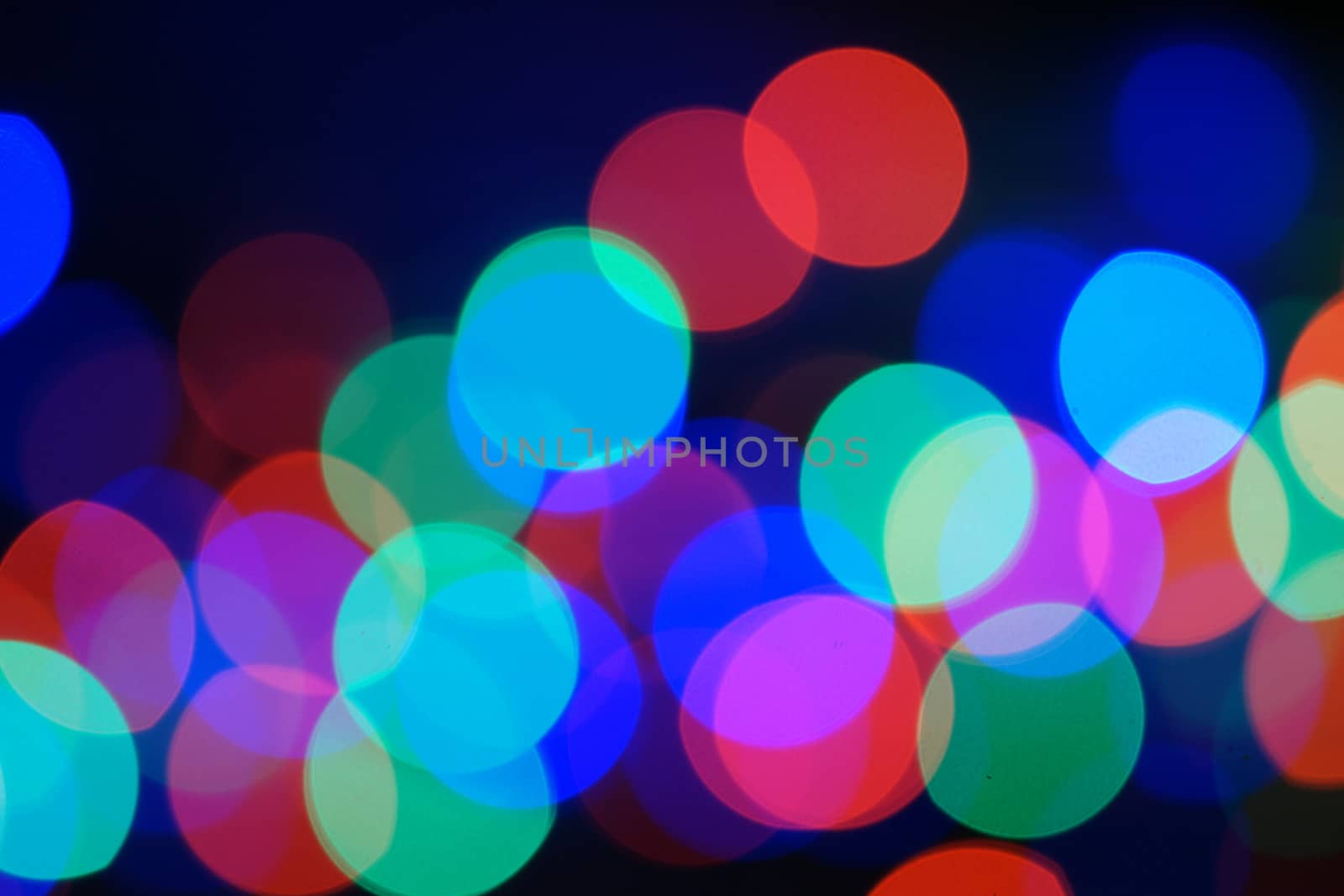 Multi-color blue holiday garland. Garland is blurred. Many big colorful round lights. Fully defocused photo. Blurred background and foreground. Holiday mood. New Year and Christmas is coming.