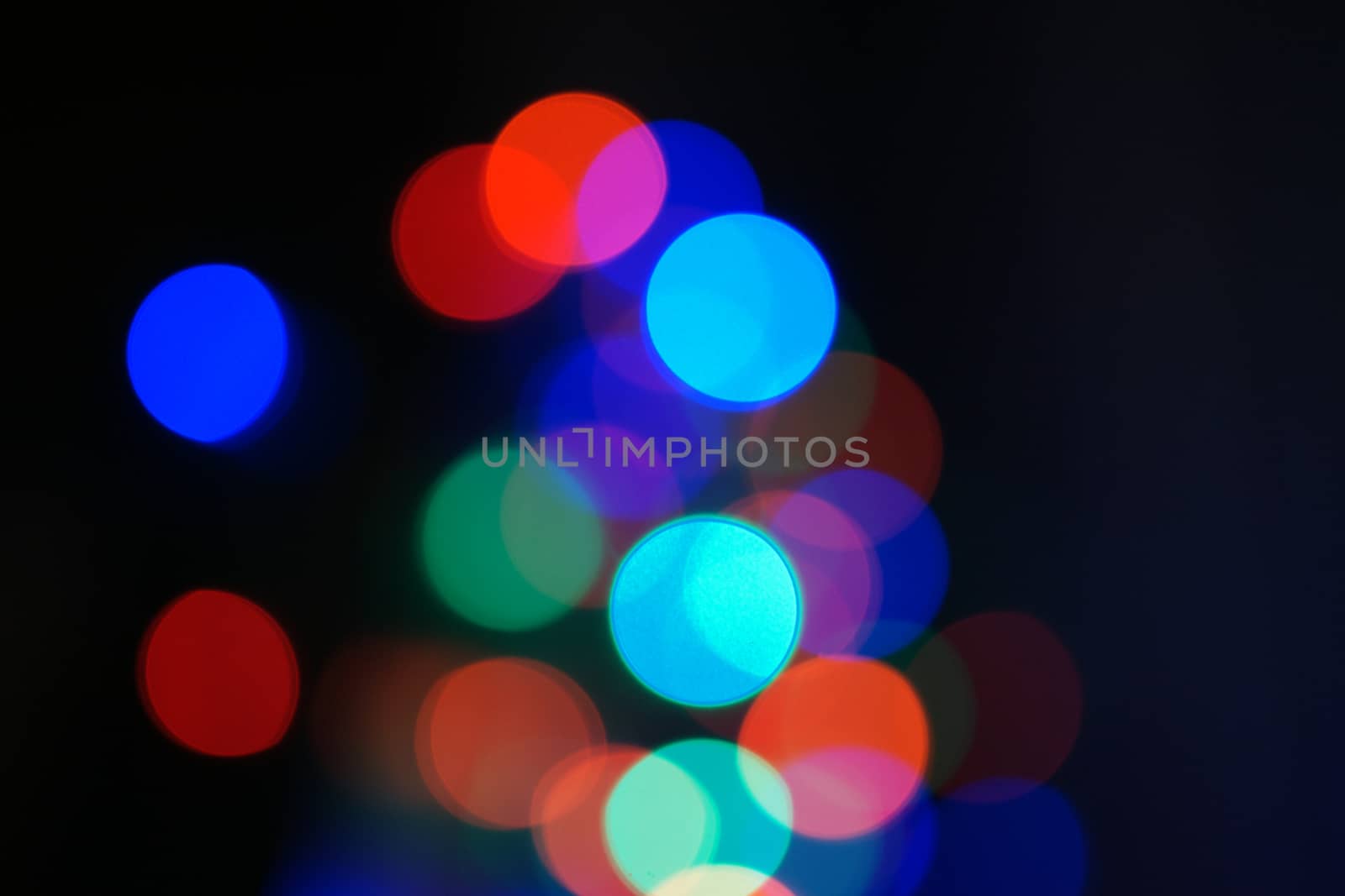 Multi-color blue holiday garland. Garland is blurred. Many big colorful round lights. Fully defocused photo. Blurred background and foreground. Holiday mood. New Year and Christmas is coming.