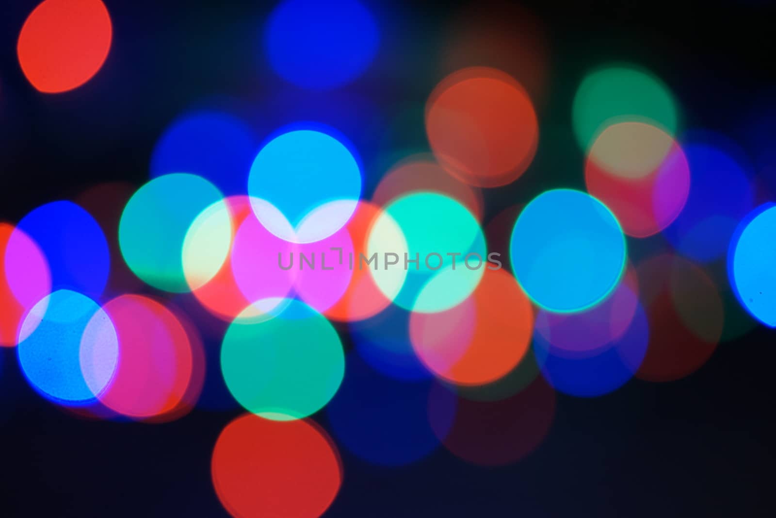 Multi-color blue holiday garland. Garland is blurred. Many big colorful round lights. Fully defocused photo. Blurred background and foreground. Holiday mood. New Year and Christmas is coming.