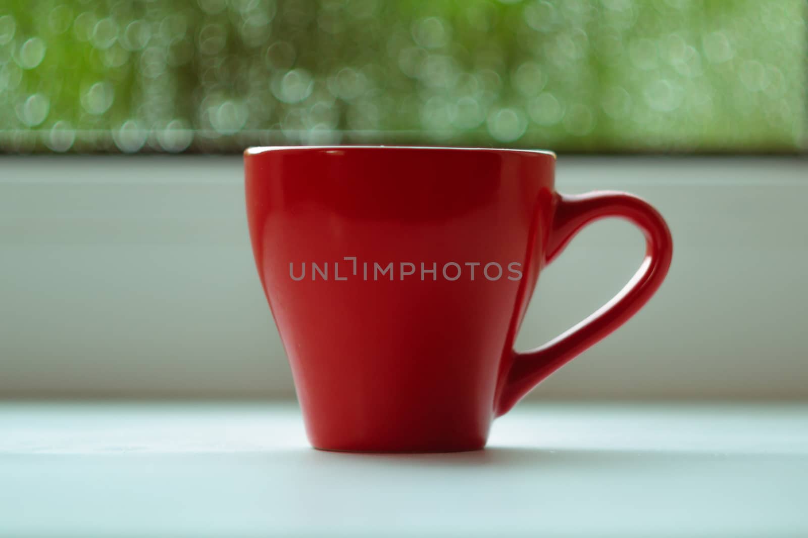 The red espresso cup on white windowsill. On background window and rain. Cup located in center of frame.