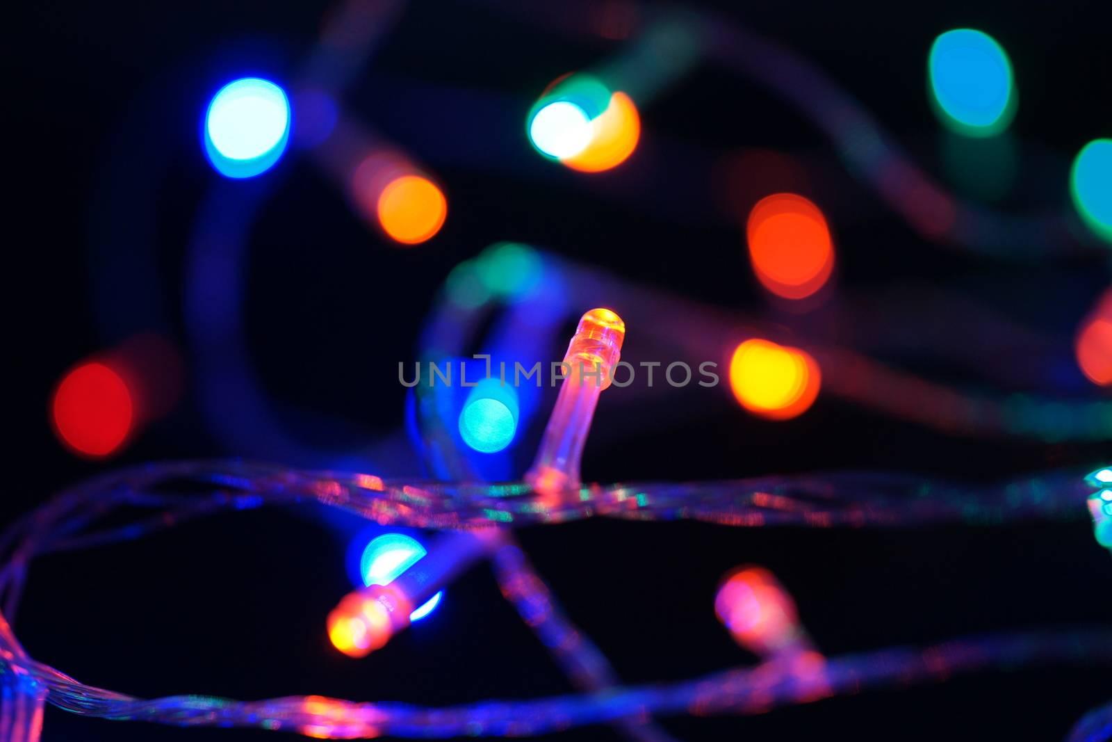 Multi-color blue holiday garland. Garland is blurred. Many big colorful round lights. Fully defocused photo. Blurred background and foreground. Holiday mood. New Year and Christmas is coming.