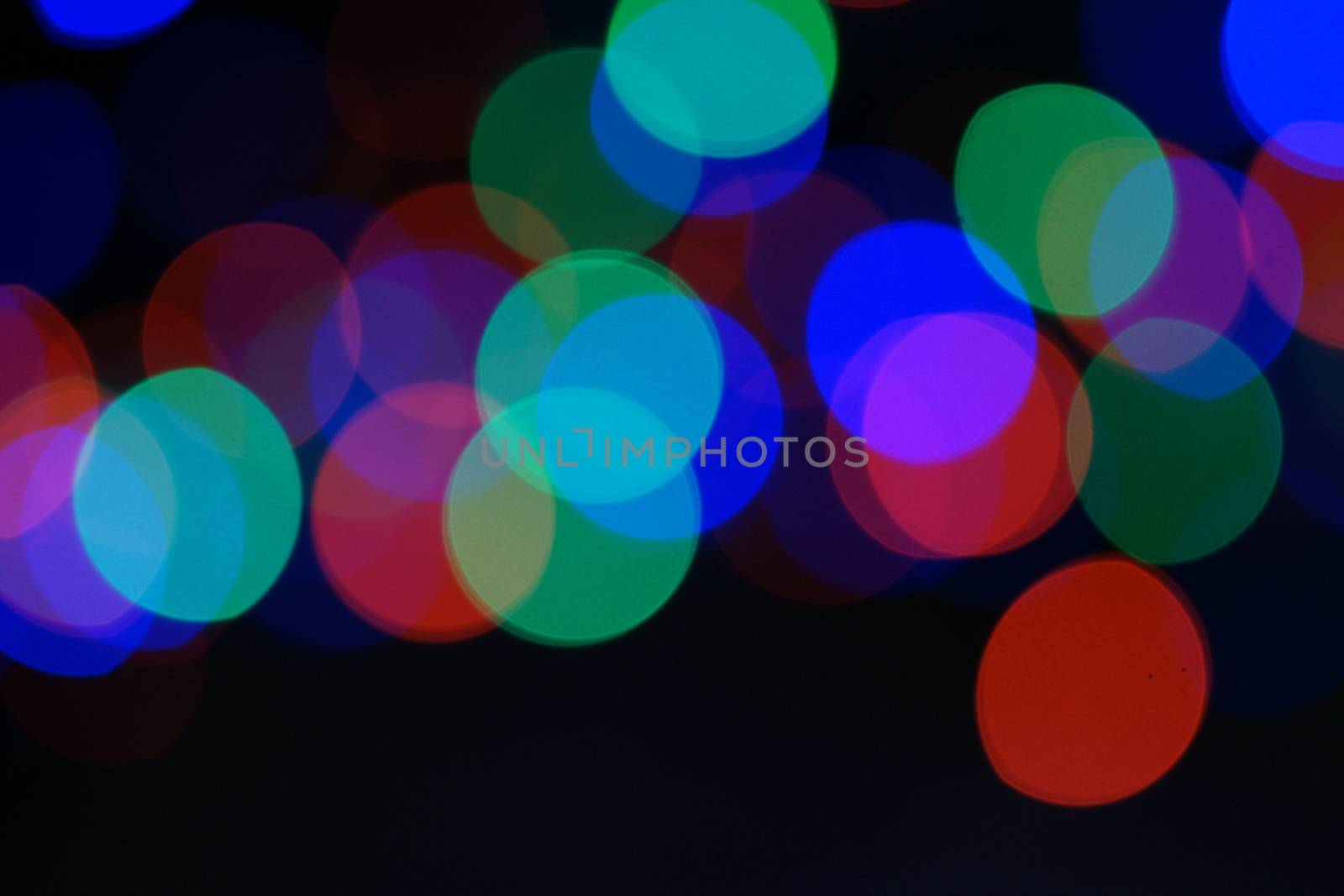 Multi-color blue holiday garland. Garland is blurred. Many big colorful round lights. Fully defocused photo. Blurred background and foreground. Holiday mood. New Year and Christmas is coming.