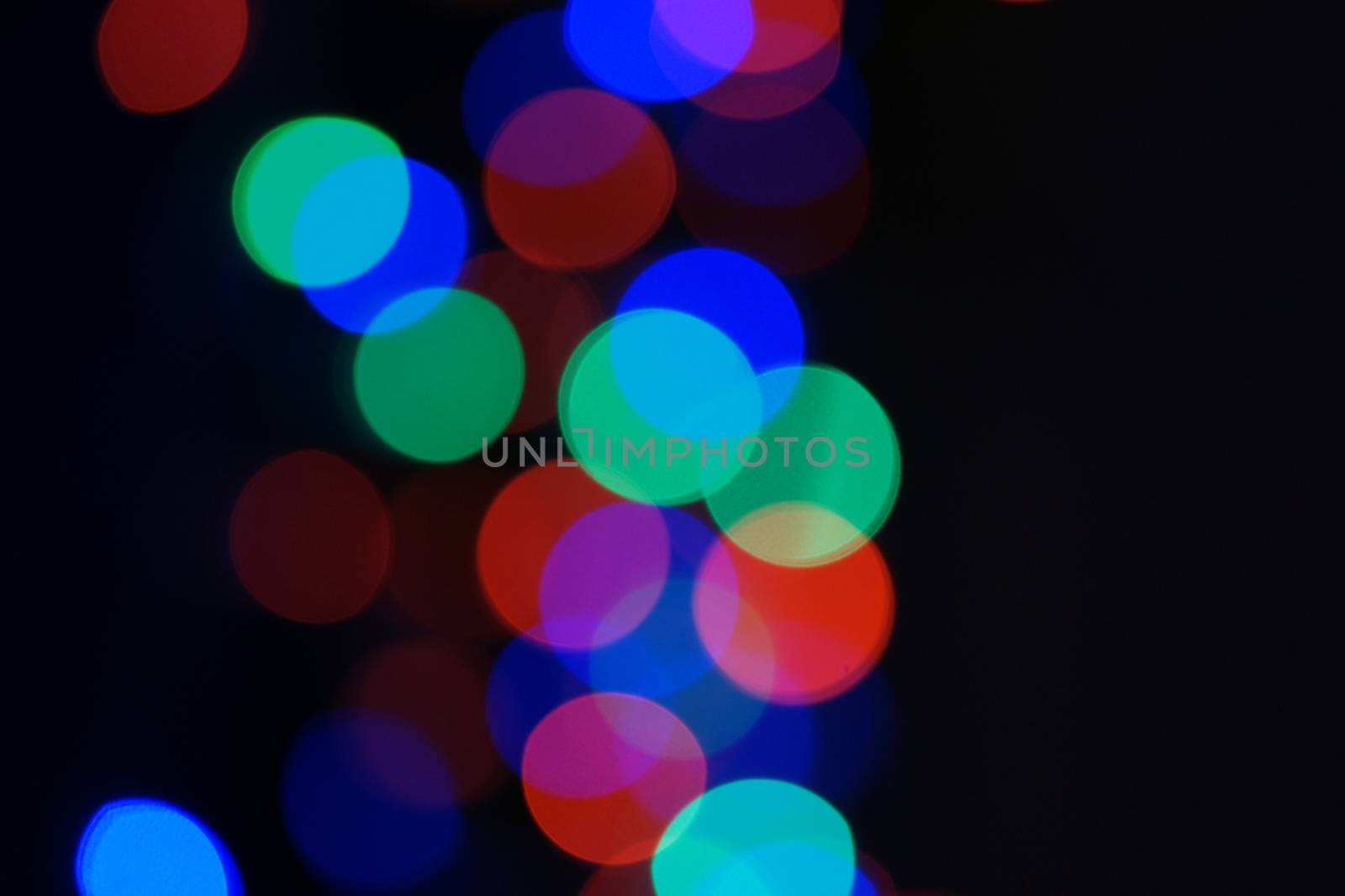 Multi-color blue holiday garland. Garland is blurred. Many big colorful round lights. Fully defocused photo. Blurred background and foreground. Holiday mood. New Year and Christmas is coming.