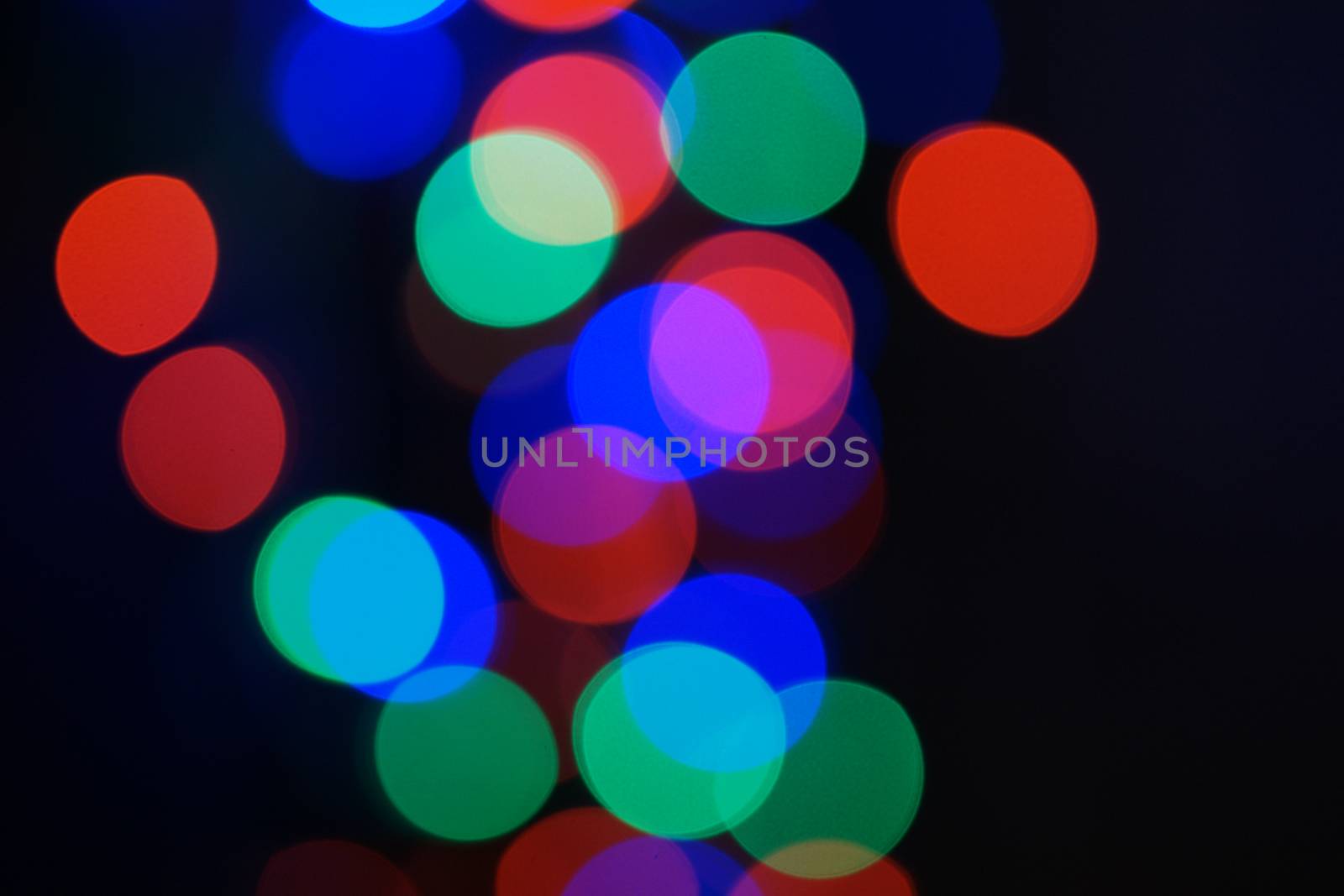 Multi-color blue holiday garland. Garland is blurred. Many big colorful round lights. Fully defocused photo. Blurred background and foreground. Holiday mood. New Year and Christmas is coming.