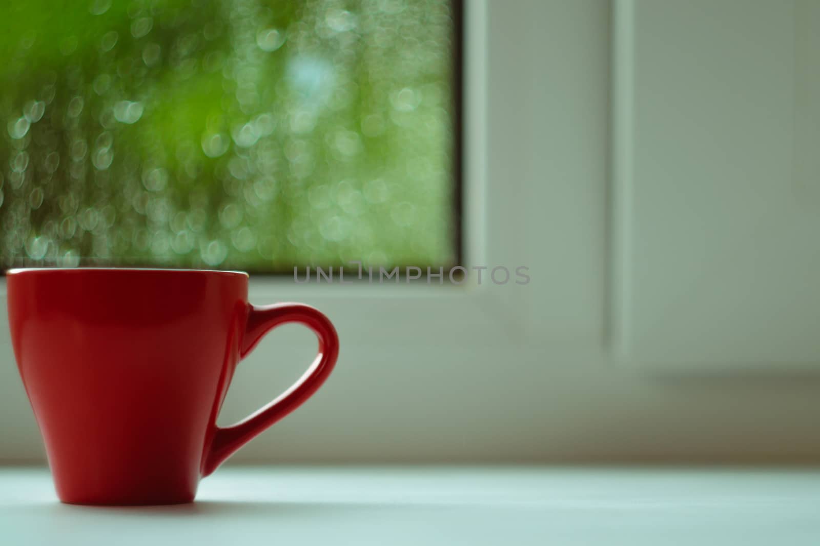 The red espresso cup on white windowsill. On background window and rain. Cup located at left of frame.