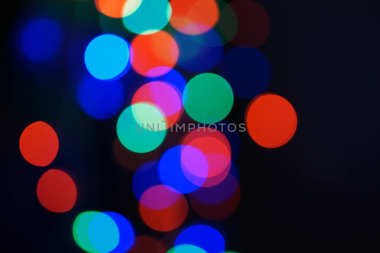 Multi-color blue holiday garland. Garland is blurred. Many big colorful round lights. Fully defocused photo. Blurred background and foreground. Holiday mood. New Year and Christmas is coming.