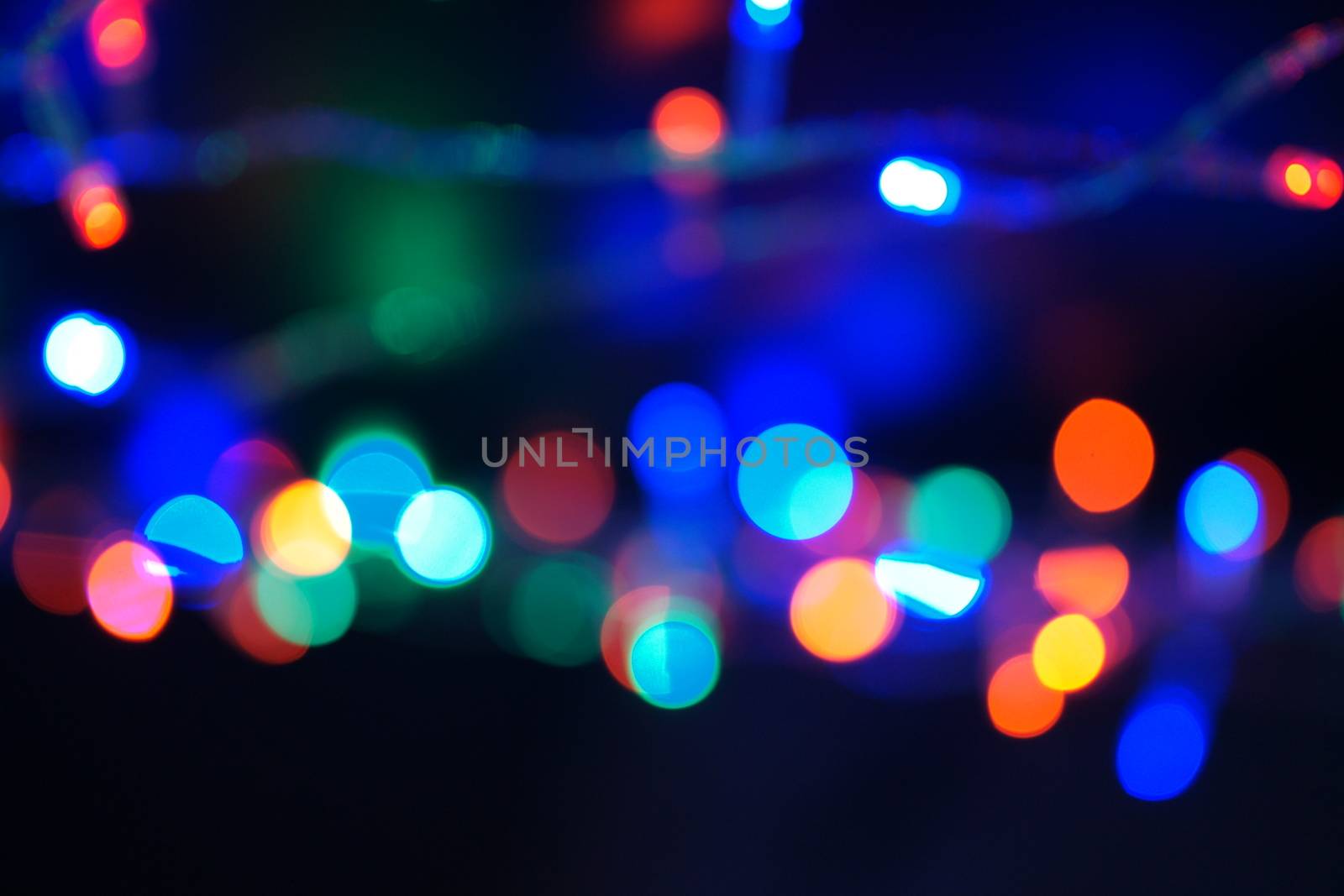 Multi-color blue holiday garland. Garland is blurred. Many big colorful round lights. Fully defocused photo. Blurred background and foreground. Holiday mood. New Year and Christmas is coming.