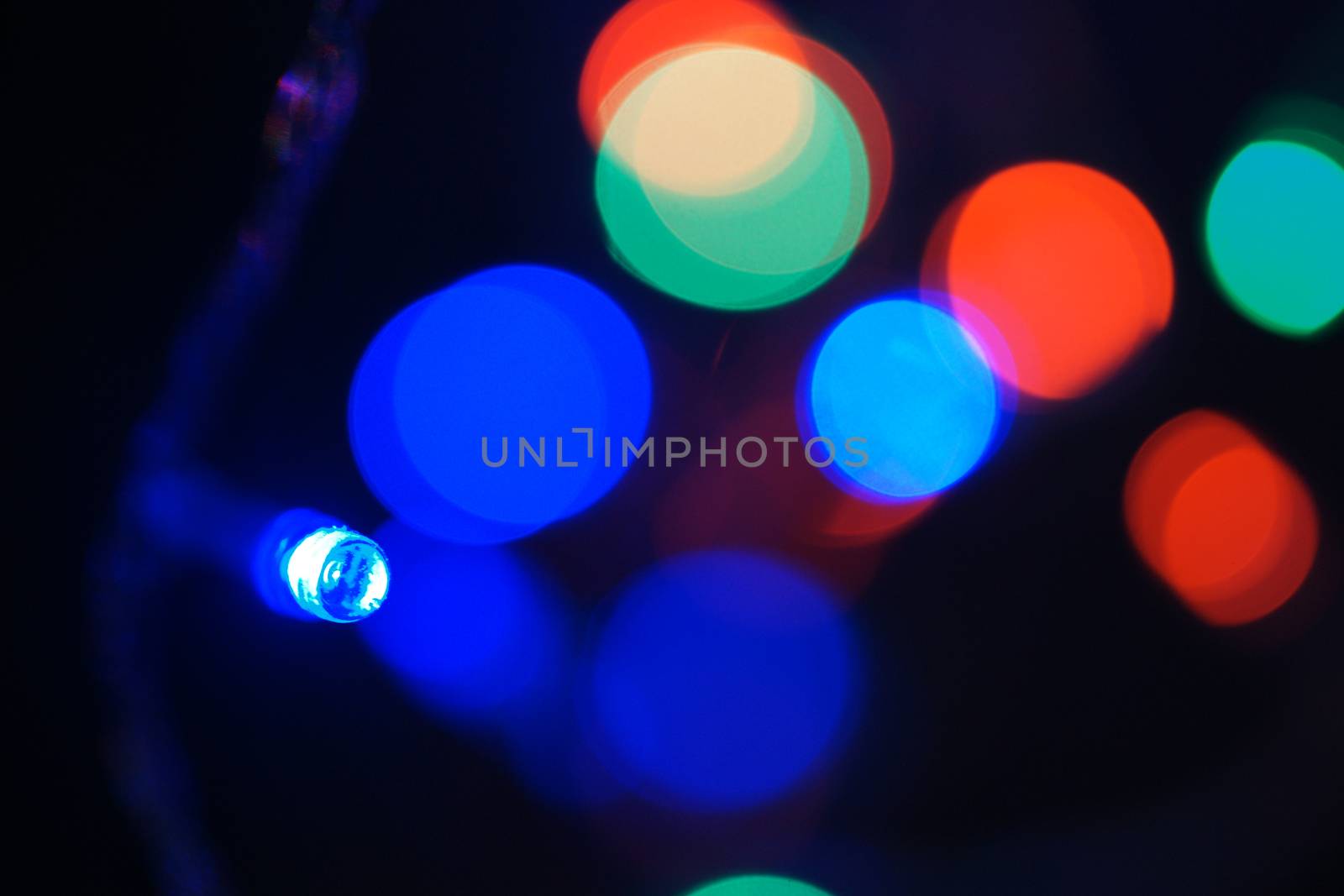 Multi-color blue holiday garland. Garland is blurred. Many big colorful round lights. Fully defocused photo. Blurred background and foreground. Holiday mood. New Year and Christmas is coming.