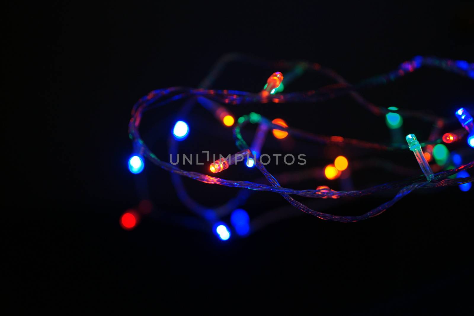 Multi-color blue holiday garland. Garland is blurred. Many big colorful round lights. Fully defocused photo. Blurred background and foreground. Holiday mood. New Year and Christmas is coming.