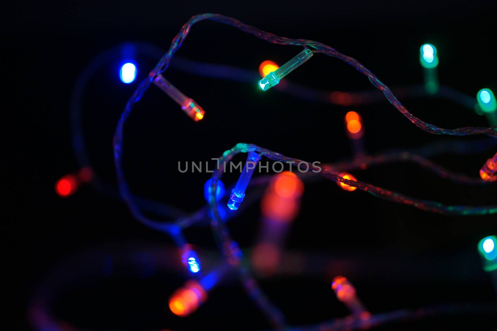 Multi-color blue holiday garland. Garland is blurred. Many big colorful round lights. Fully defocused photo. Blurred background and foreground. Holiday mood. New Year and Christmas is coming.