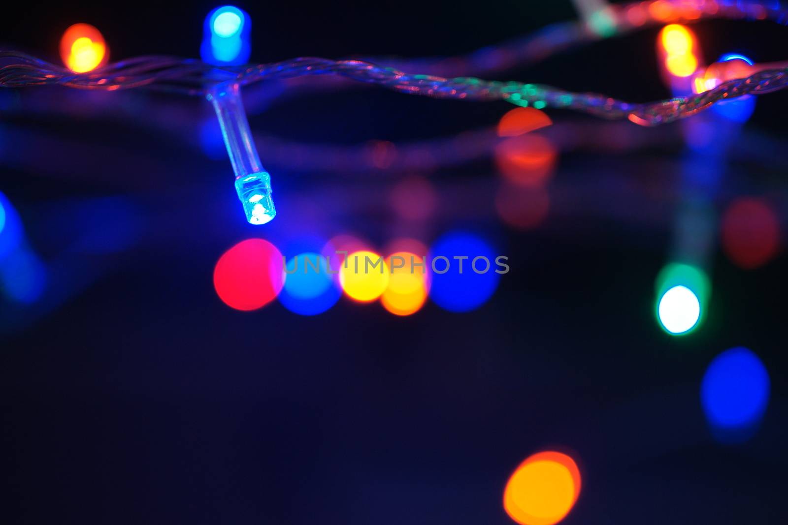 Multi-color blue holiday garland. Garland is blurred. Many big colorful round lights. Fully defocused photo. Blurred background and foreground. Holiday mood. New Year and Christmas is coming.