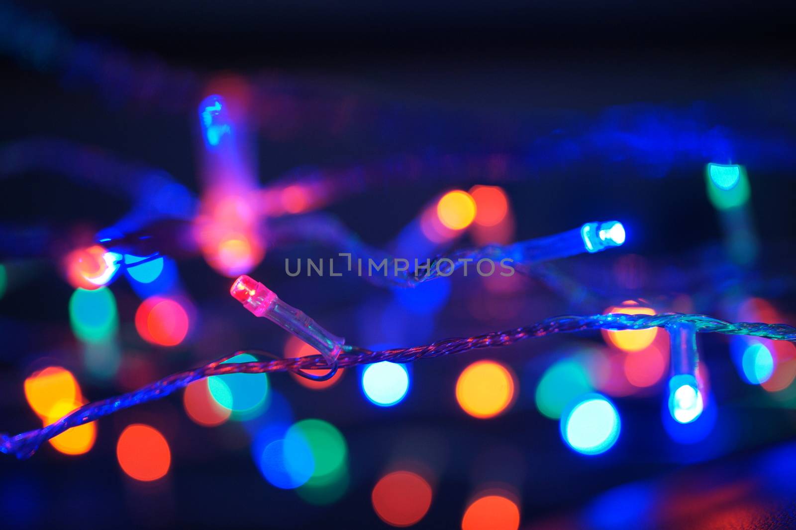 Multi-color blue holiday garland. Garland is blurred. Many big colorful round lights. Fully defocused photo. Blurred background and foreground. Holiday mood. New Year and Christmas is coming.