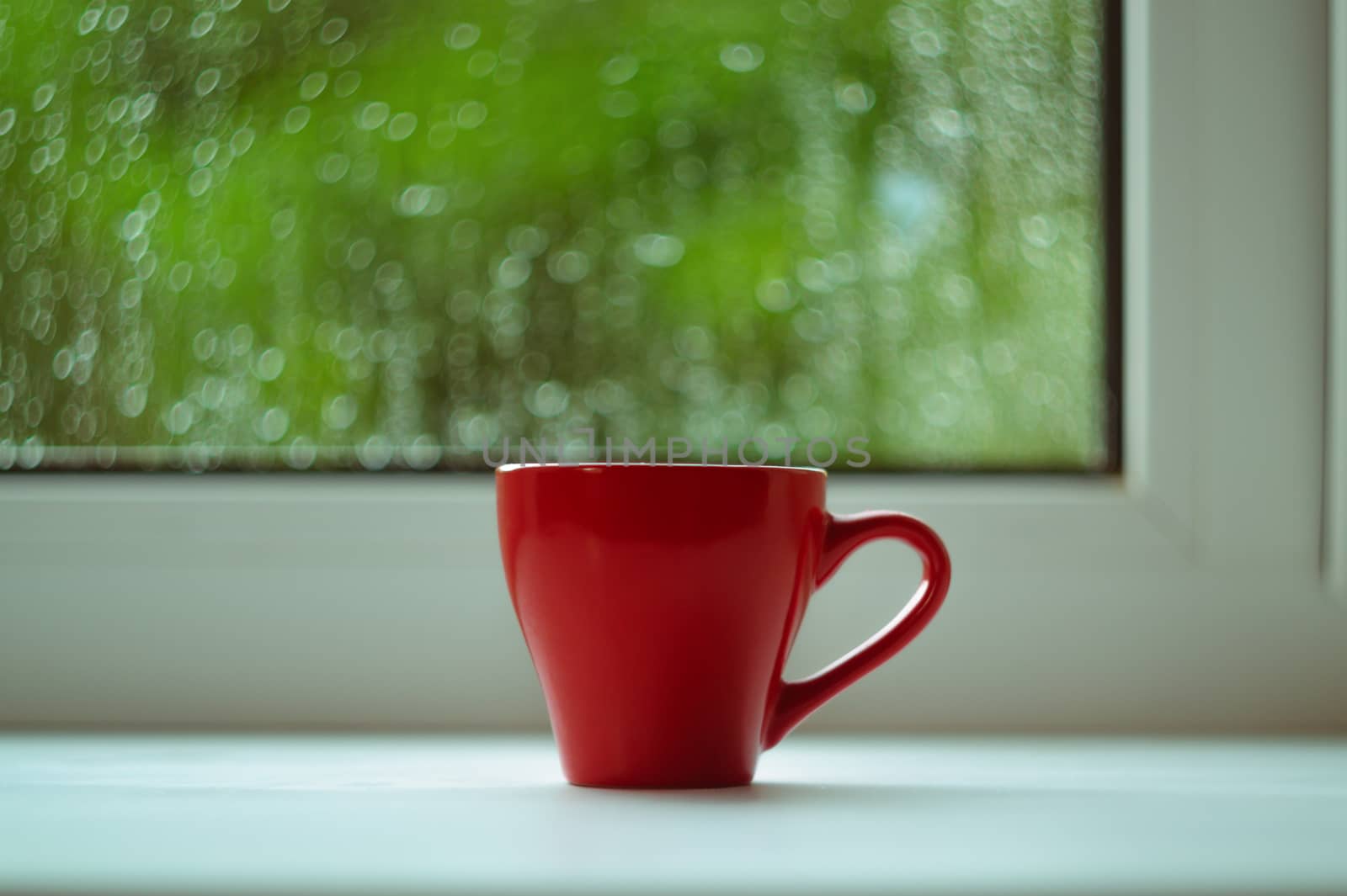 The red espresso cup on white windowsill. On background window and rain. Cup located in center of frame.
