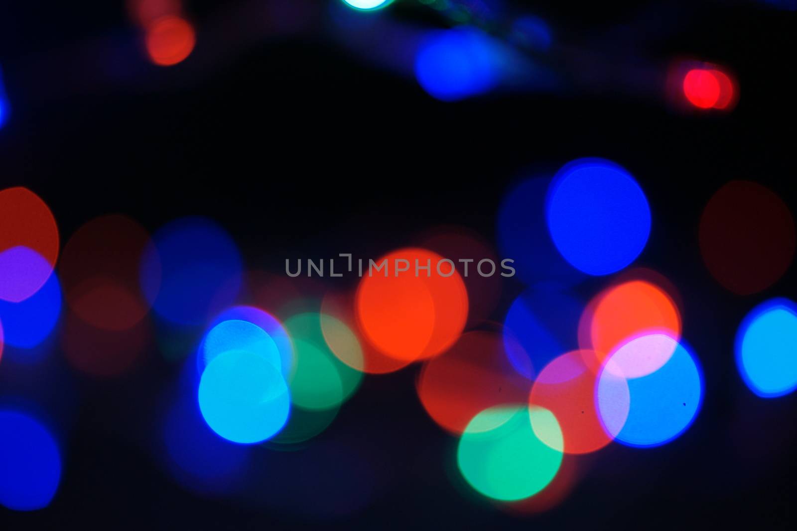 Multi-color blue holiday garland. Garland is blurred. Many big colorful round lights. Fully defocused photo. Blurred background and foreground. Holiday mood. New Year and Christmas is coming.