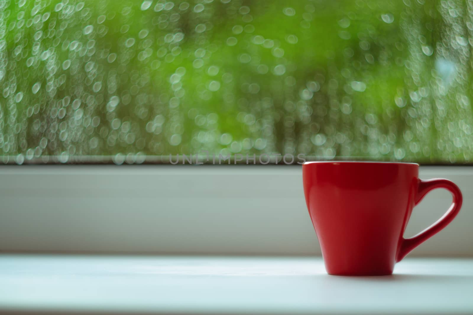 The red espresso cup on white windowsill. On background window and rain. Cup located at right of frame.