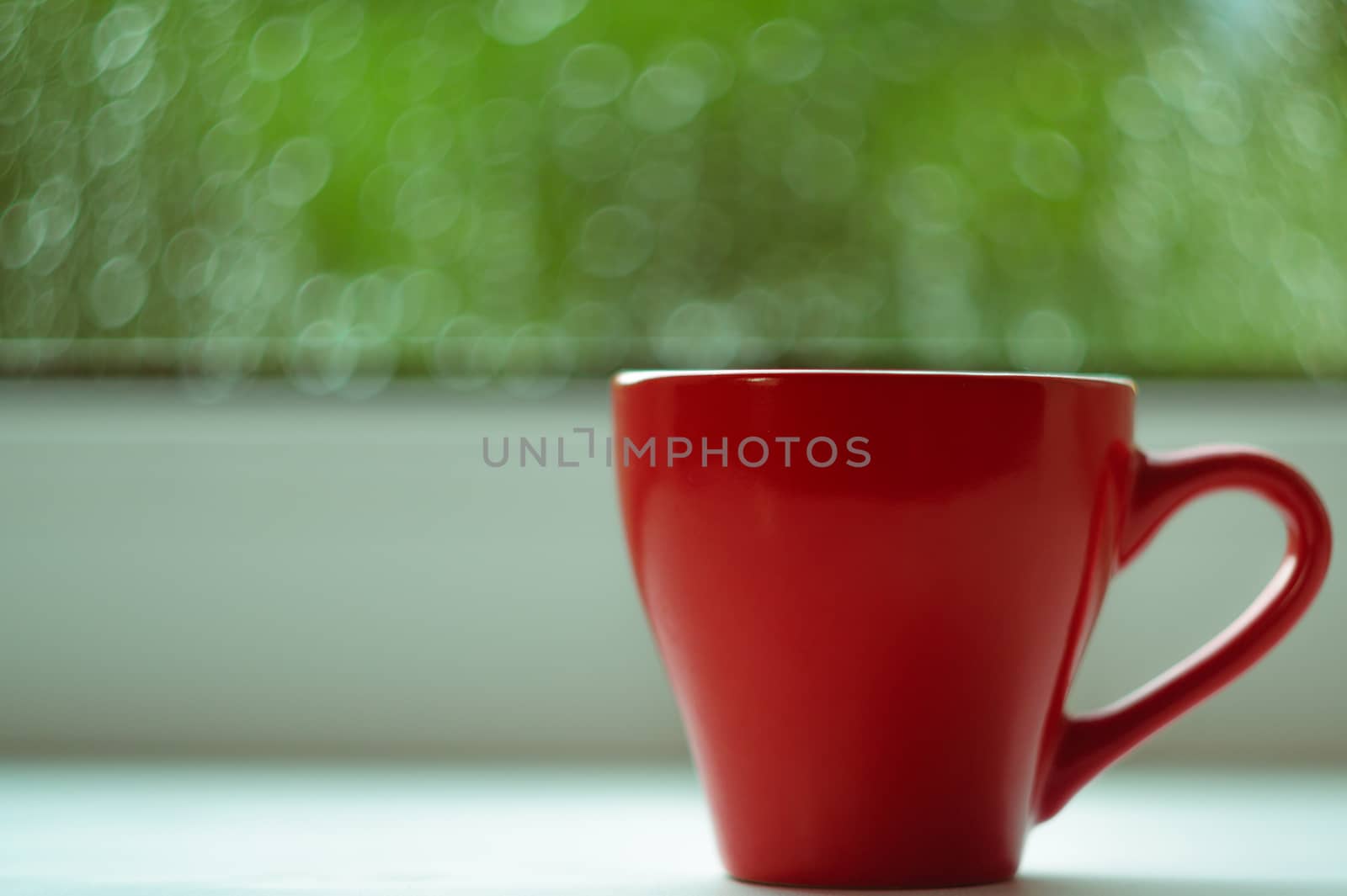 The red espresso cup on white windowsill. On background window and rain. Cup located at right of frame.
