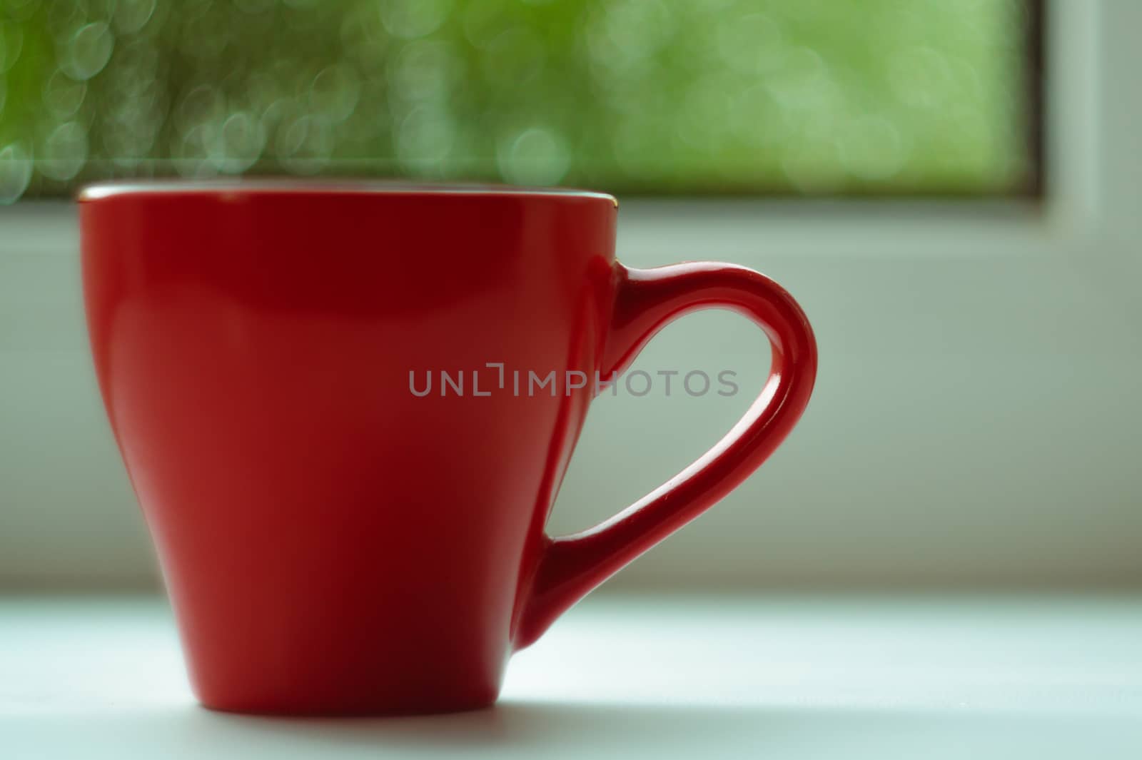 The red espresso cup on white windowsill. On background window and rain. Cup located at left of frame.