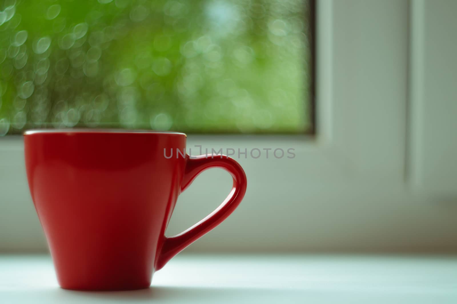 The red espresso cup on white windowsill. On background window and rain. Cup located at left of frame.