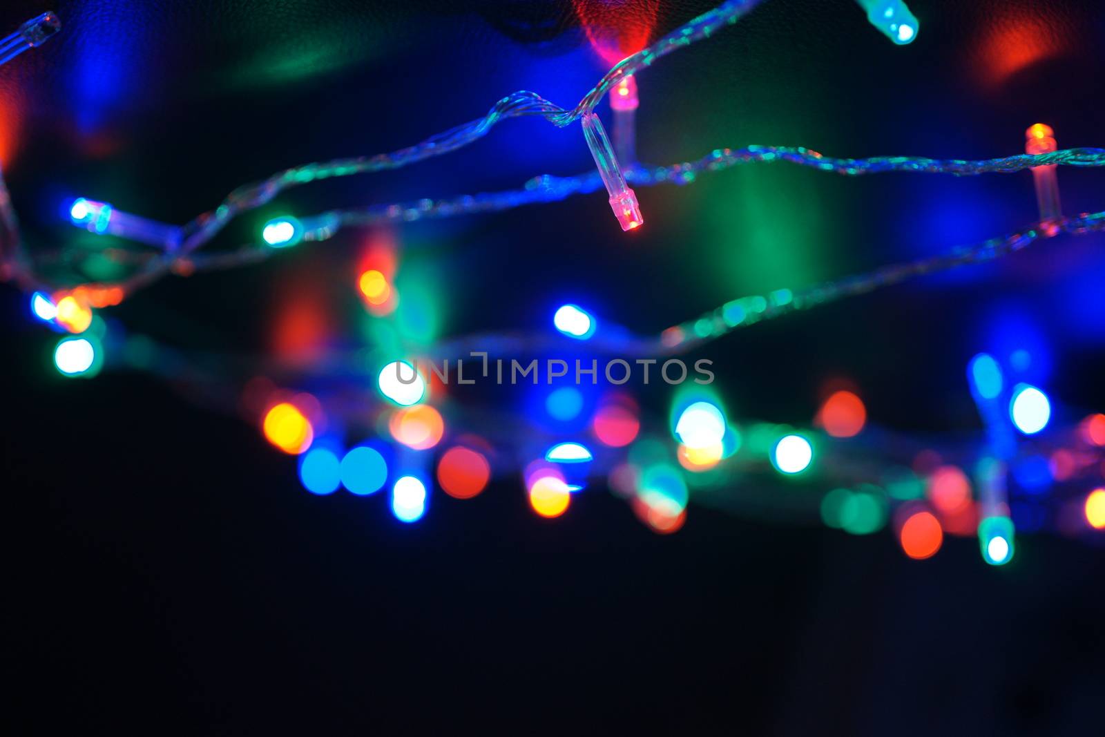 Multi-color blue holiday garland. Garland is blurred. Many big colorful round lights. Fully defocused photo. Blurred background and foreground. Holiday mood. New Year and Christmas is coming.