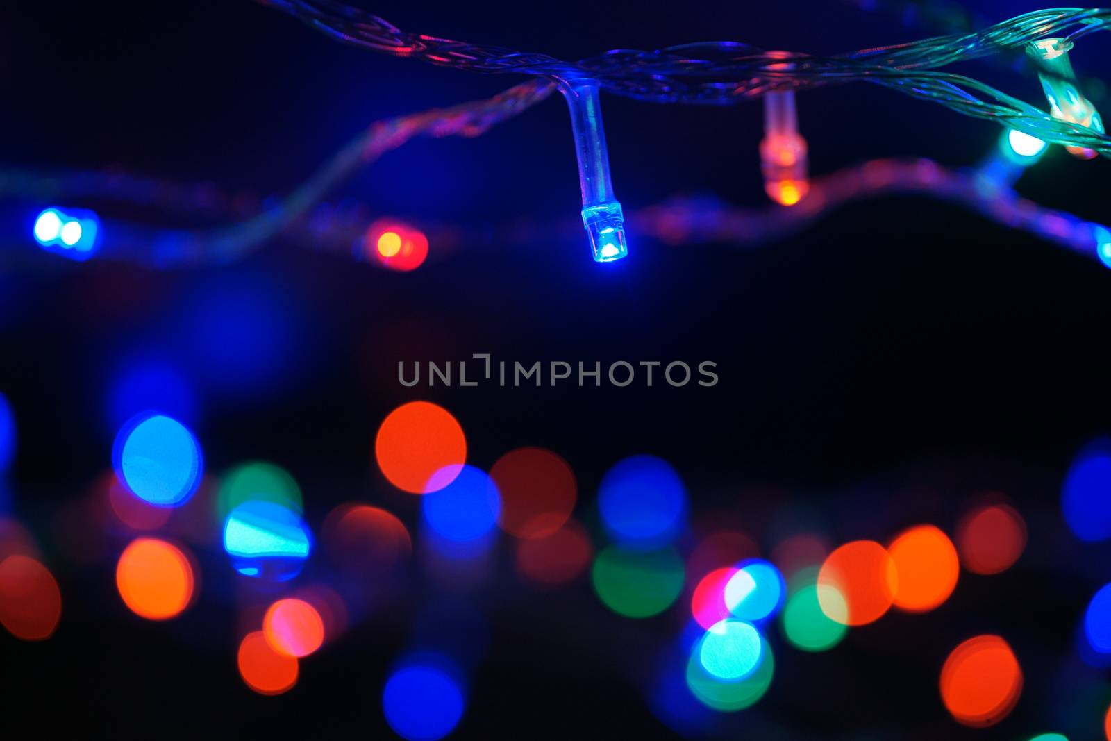 Multi-color blue holiday garland. Garland is blurred. Many big colorful round lights. Fully defocused photo. Blurred background and foreground. Holiday mood. New Year and Christmas is coming.