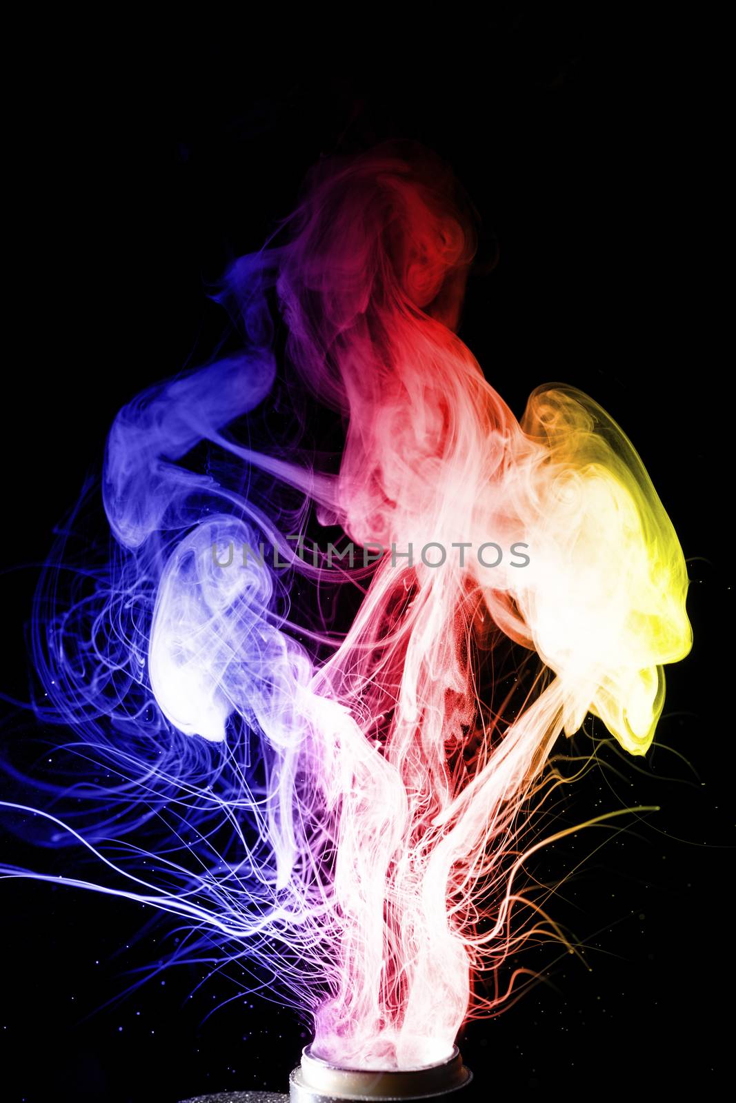 Male hand holds vape. Vape clouds splash from coil on black background. Fog is blue red and yellow colours. Stock isolated smoke with spray boiling glycerine.