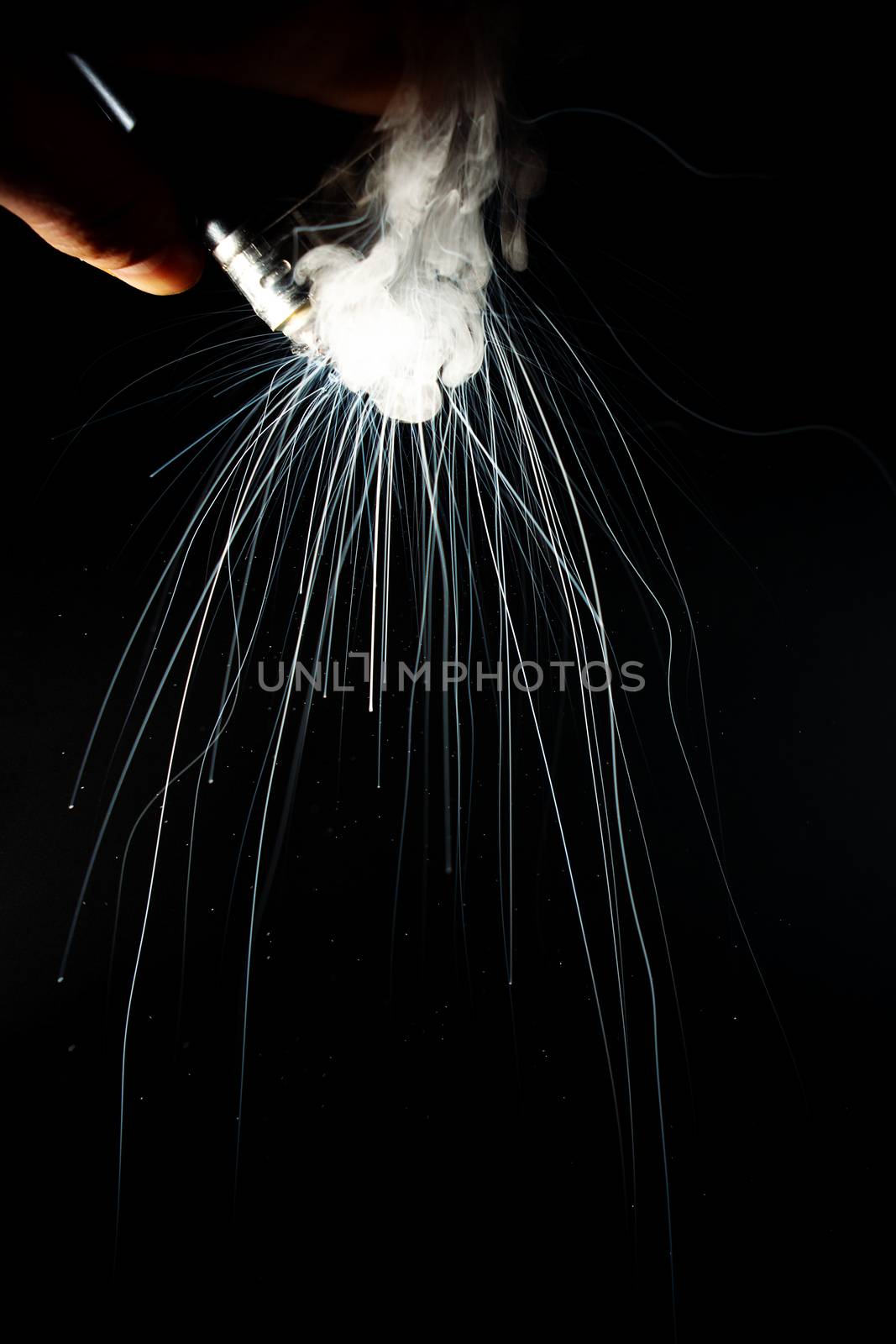 Male hand holds vape upside down. Vape clouds splash from coil on black background. Fog is white. Stock isolated white smoke with spray boiling glycerine.