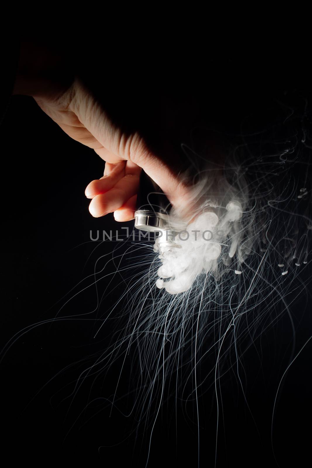 Male hand holds vape upside down. Vape clouds splash from coil on black background. Fog is white. Stock isolated white smoke with spray boiling glycerine.