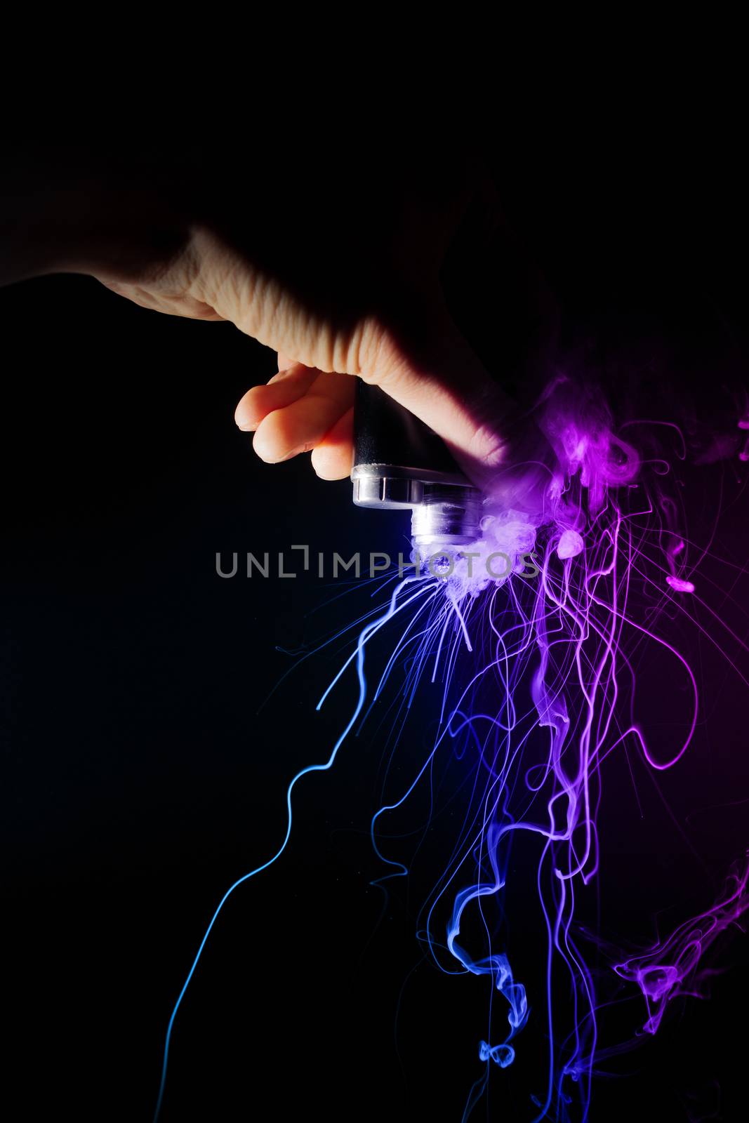 Male hand holds vape upside down. Vape clouds splash from coil on black background. Fog is two-colour blue and purple. Stock isolated dual color smoke with spray boiling glycerine.