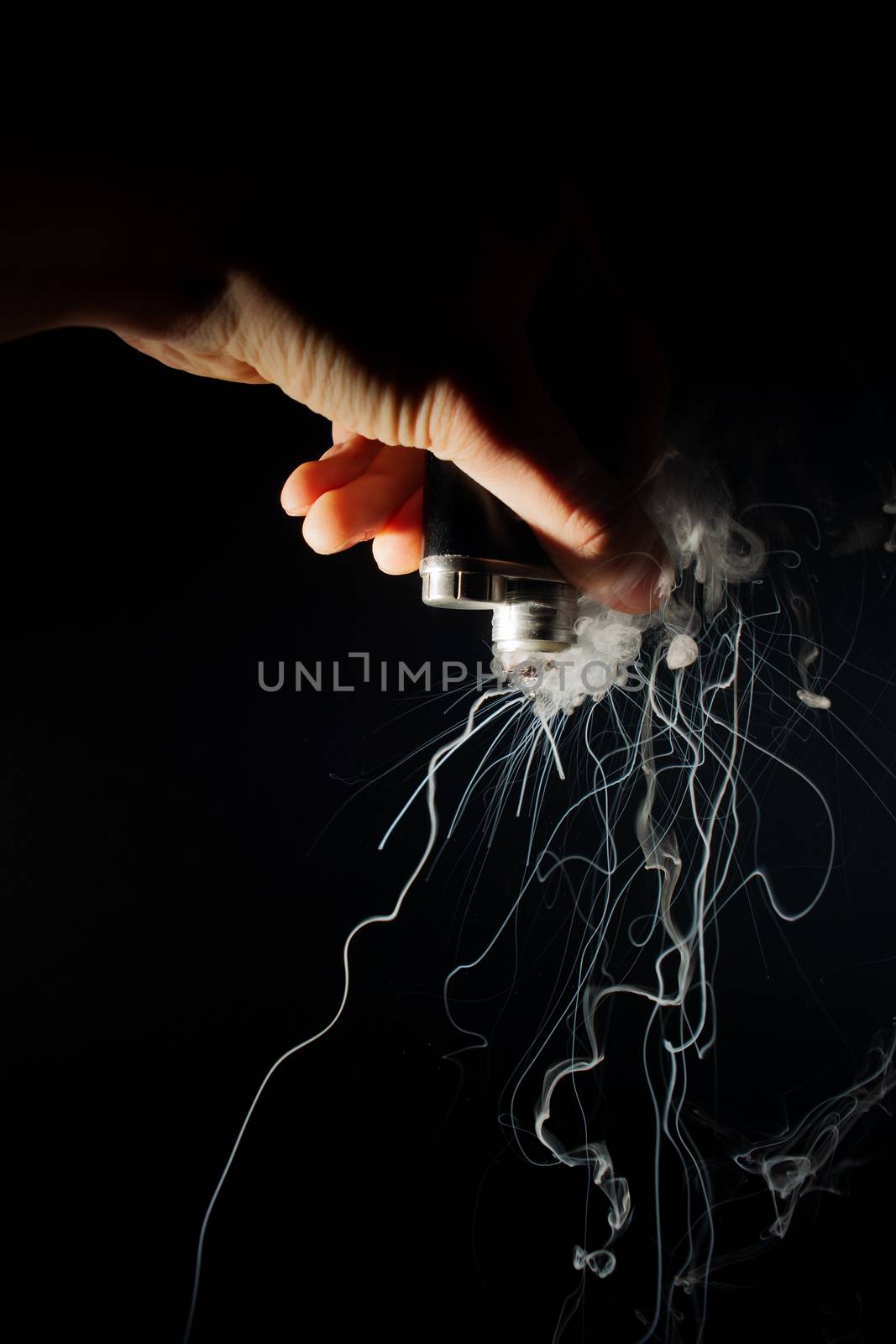 Male hand holds vape upside down. Vape clouds splash from coil on black background. Fog is white. Stock isolated white smoke with spray boiling glycerine.