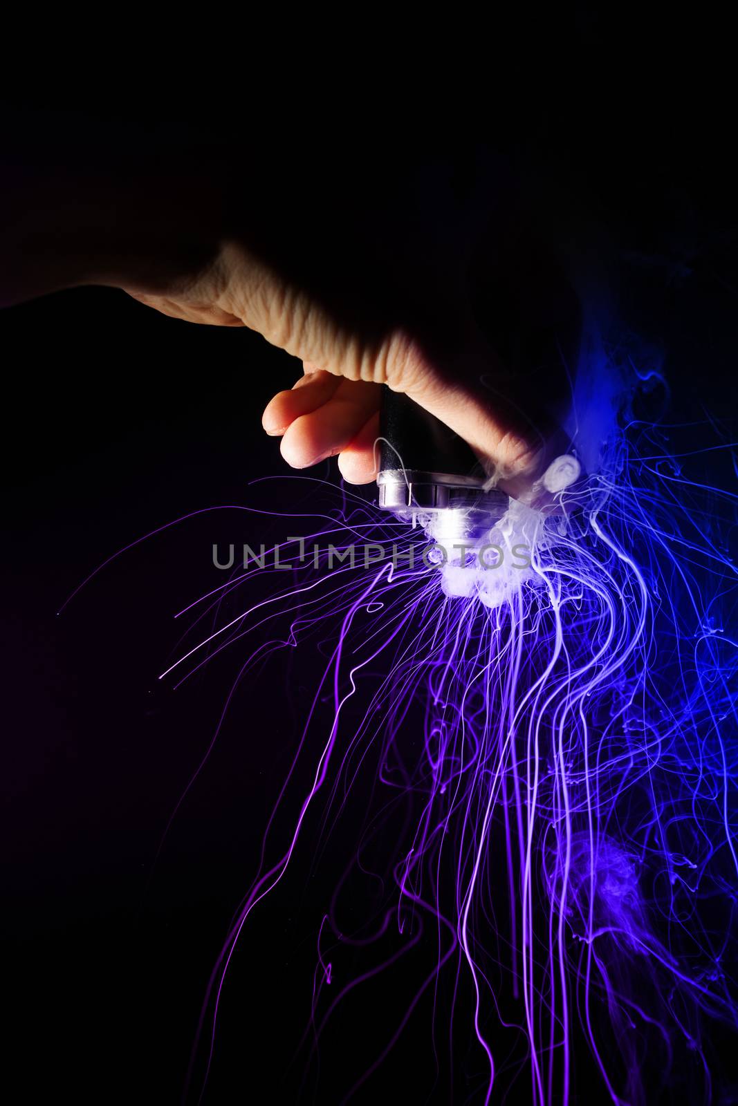 Male hand holds vape upside down. Vape clouds splash from coil on black background. Fog is two-colour blue and purple. Stock isolated dual color smoke with spray boiling glycerine.