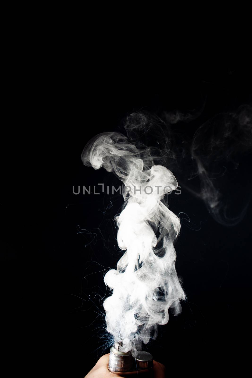 Man hand holds vape. Vape clouds splash from coil on black background. Fog is white. Stock isolated white smoke with spray boiling glycerine around.