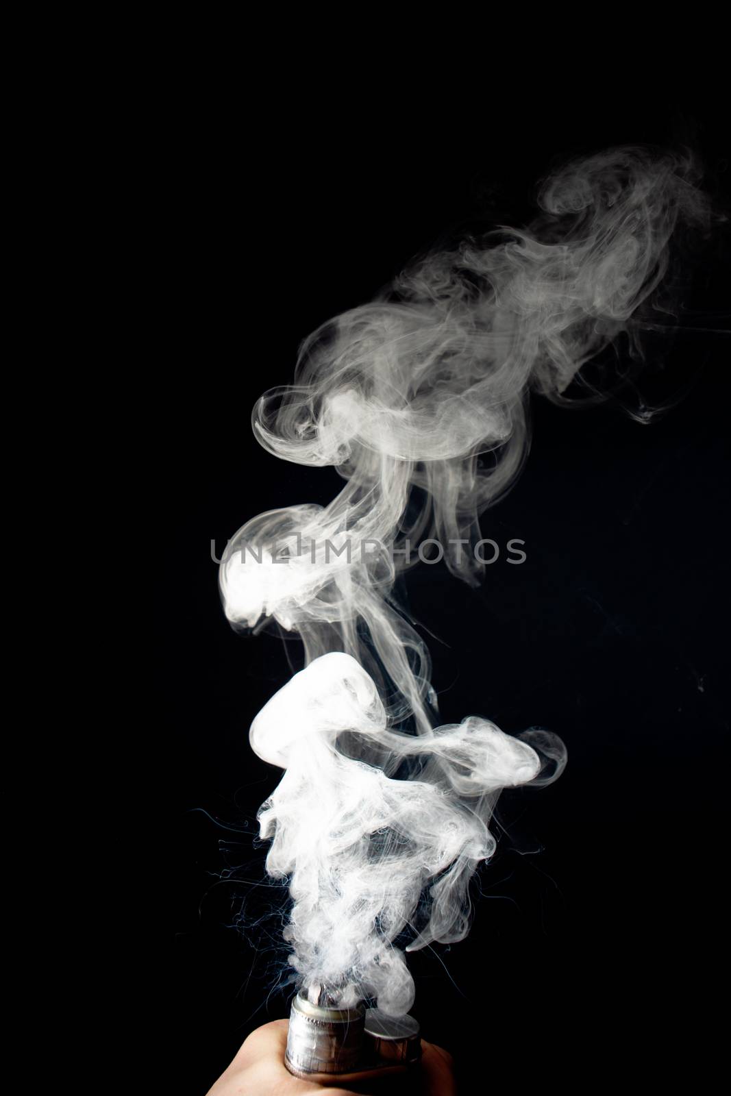 Male hand holds vape without atomiser. Column of vape clouds splash from coil on black background. Fog is white. Stock isolated white smoke with spray boiling glycerine.