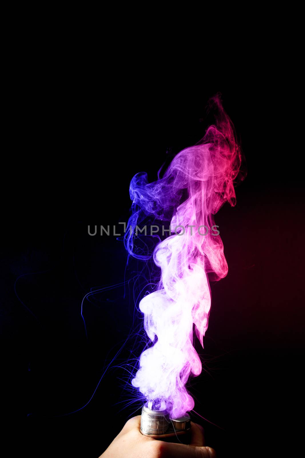 Male hand holds vape. Vape clouds splash from vape coil on black background. Fog is dual color — blue and red. Stock isolated dual colour smoke with spray boiling glycerine.