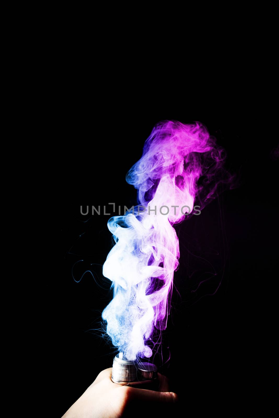 Young man holds vape in his hand. Vape clouds splash from vape coil on black background. Fog is dual color — blue and purple. Stock isolated colorful smoke with spray boiling glycerine.